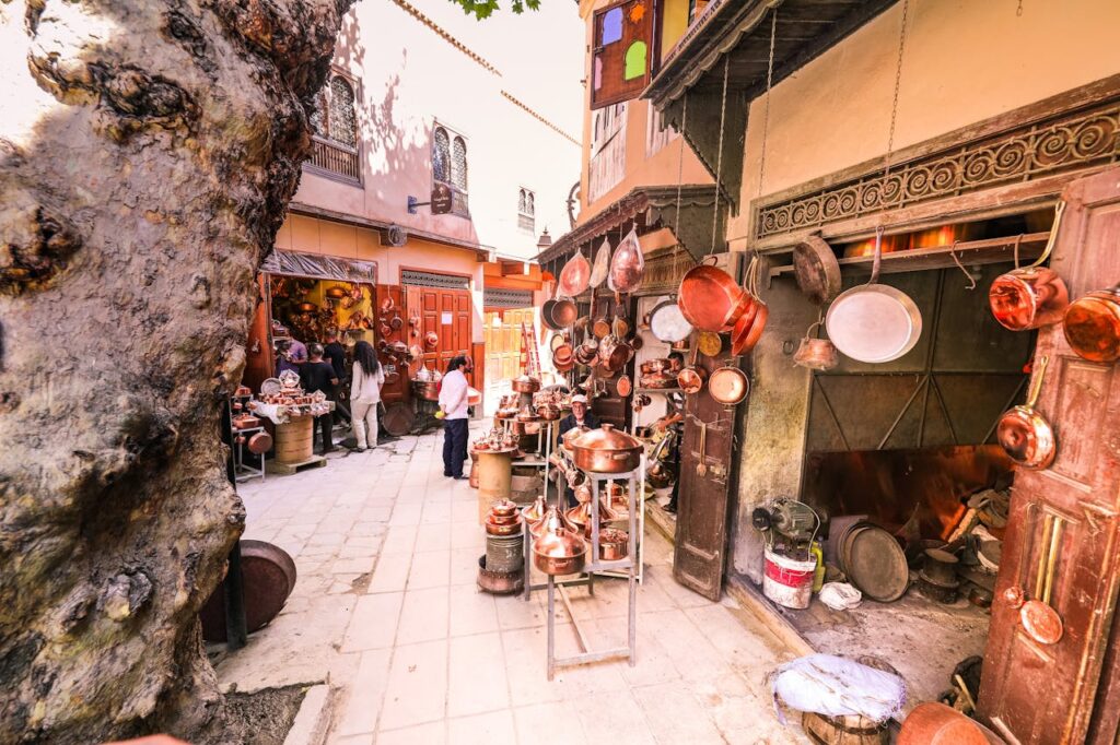 A vibrant outdoor market scene displaying hanging brass pots and people shopping.